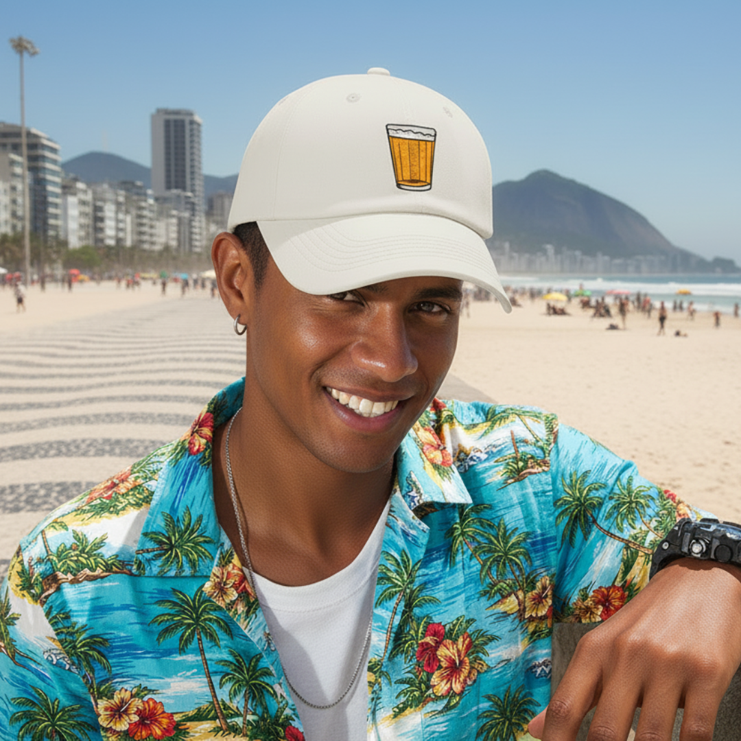 Man wearing a white cap with a beer mug design on a beach with a cityscape in the background