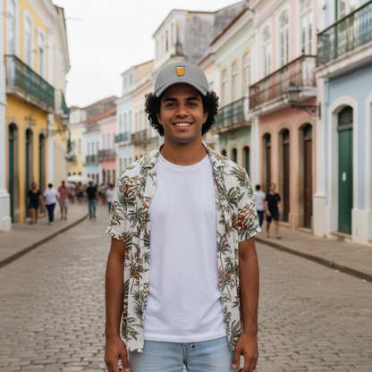 Man standing on a street with colorful buildings in the background. He's wearing a grey hat with a glass of "cervejinha."